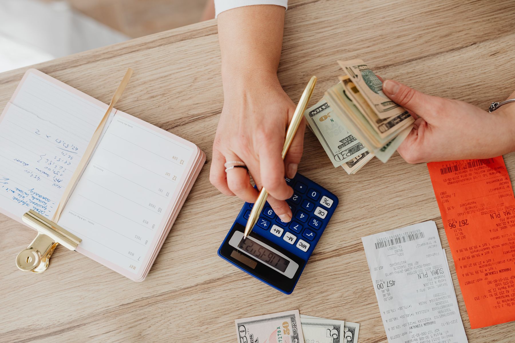 Hands using a calculator beside cash and household receipts